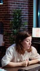 Poster - Vertical video Tired employee struggling to remain focused at workspace desk, feeling overworked and waiting to go home. Bored businesswoman sighing in office while working overnight, camera A