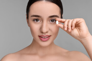 Poster - Beautiful young woman with vitamin pill on grey background