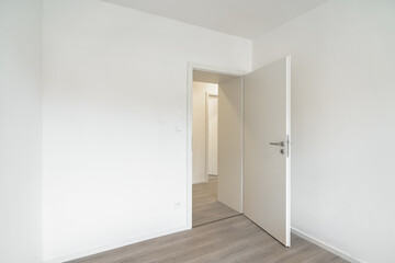 Wall Mural - An Empty, bright room with white walls and a wooden floor. An open door leads to another similar room.