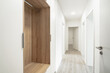 A Clean, modern hallway with wooden floors, white walls, an open wooden closet, and opened doors. It’s bright and inviting.