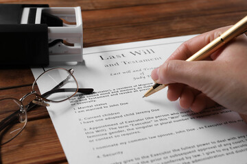 Poster - Woman signing Last Will and Testament at wooden table, closeup