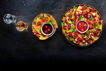 Poster - Loaded nachos. Mexican nacho chips with beef, overhead flat lay shot with guacamole sauce, cheese salsa, chili and jalapenos, tequila drinks, on a black slate background