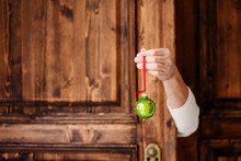 Hand Holding Green Christmas Bauble In Front Of Wooden Door
