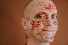 Smiling Face Of Drag Queen With Red Glitter On Face Against Brown Background
