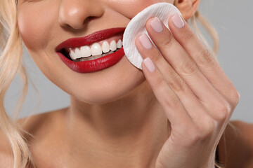 Wall Mural - Smiling woman removing makeup with cotton pad on light grey background, closeup