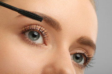 Wall Mural - Woman applying mascara on grey background, closeup