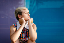 Portrait Of Female Teenager With Closed Eyes Wearing Colorful Dress With Multicolored Glass Wall In The Background