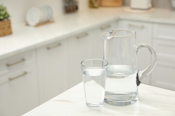 Poster - Jug and glass with clear water on white table in kitchen, space for text