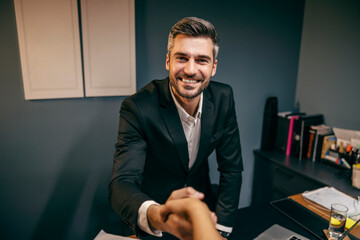 A businessman is shaking hands with business partner at his office.