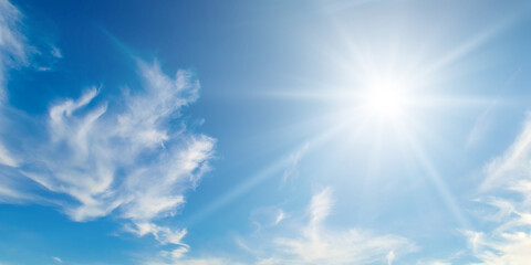 Wall Mural - There are light white clouds and bright sun in the blue sky. Wide photo.