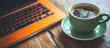 a green cup of coffee sits beside a laptop in