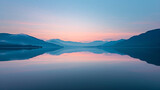 Fototapeta Na ścianę - A calm lake reflecting the surrounding mountains and sky at dawn.