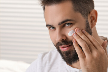 Poster - Man with dry skin applying cream onto his face on light background, space for text