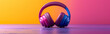 Purple headphones isolated on a vibrant pink and orange background. minimalist panoramic header. Presentation of the wireless audio technology for listening to music on a blank colourful wide banner