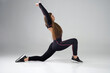 Flexible female in activewear stretching body in Crescent Lunge pose of yoga in studio. Side view of Caucasian woman with long hair practicing yoga asana on floor, isolated on grey. Yoga concept.