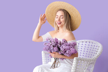 Poster - Young woman with lilac flowers in armchair on color background