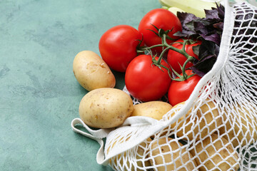 Mesh bag with different fresh vegetables on green background, closeup