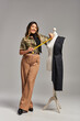 © LIGHTFIELD STUDIOS - young asian clothes designer holding measuring tape near mannequin with fabric on grey backdrop
