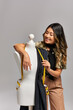 © LIGHTFIELD STUDIOS - pleased asian designer posing near mannequin with fabric and measuring tape on grey backdrop