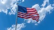 A proud American stars and stripes flag flies from a mast with a blue sky and clouds in the background.