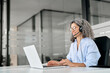 © insta_photos - Happy senior older woman professional call contact center agent wearing headset hybrid working in business office. Smiling middle aged female support service operator talking to customer sit at desk.