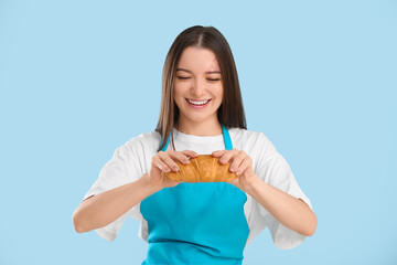 Canvas Print - Pretty young woman in apron with fresh croissant on blue background