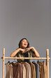 © LIGHTFIELD STUDIOS - overjoyed asian clothes stylist laughing near rack with fashionable clothes on grey backdrop