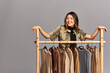 © LIGHTFIELD STUDIOS - talented delighted asian fashion designer smiling near rack with bespoke clothes on grey backdrop