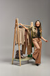 © LIGHTFIELD STUDIOS - overjoyed asian stylist smiling near rack with bespoke clothes on grey backdrop, fashion business