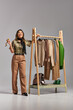 © LIGHTFIELD STUDIOS - cheerful asian stylist with measuring tape looking at camera near rack with bespoke clothes on grey