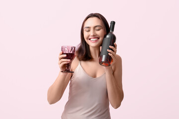 Poster - Beautiful young woman with glass and bottle of red wine on pink background