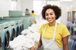 © Garnar - Cheerful Young African American woman worker professionally handling laundry duties in a bright modern laundromat. Washing concept