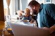 © Davor - Young single father using a laptop with his baby toddler son next to him at home