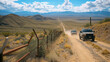  Border patrol vehicles kick up dust on a dirt road running parallel to a security fence in the desert.