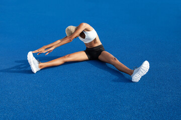 Wall Mural - An African American female athlete engages in warm-up exercises, sitting on the Olympic blue track, embodying the concept of race training and dedication in sports