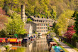  Hebden Bridge, West Yorkshire, UK - Sunny day in spring, with Rochdale Canal, leafy trees, old mill buildings, reflections, chimney, narrow boats and people walking on tow path. Beautiful.