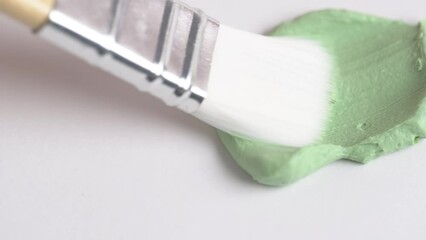 Wall Mural - Texture of green clay mask. Swatch of clay mask. Makeup brush applying green facial mask on white background.