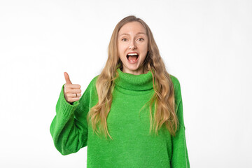 Wall Mural - Enthusiastic blonde woman shows thumb up, recommends smth good, approve and like brand or company, stands in green cozy sweater over white background