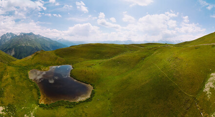 Wall Mural - Aerial view at the Koruldi lakes. Green hills, high mountain pastures. Summer day. in the background are the snowy peaks of the Caucasus Mountains. High resolution panorama