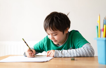 Wall Mural - Education concept,School kid using black colour pen drawing or sketching on paper,Portrait boy siting on table doing homework in living room,Child enjoy art and craft activity at home