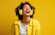 happy young woman wearing headphones laughing against yellow background