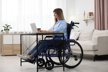 Wall Mural - Woman in wheelchair using laptop at table in home office