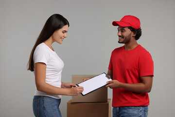 Poster - Smiling woman signing order receipt on grey background. Courier delivery