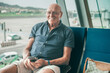 © luciano - Smiling senior bald man sitting in airport departure area waiting for boarding. Travel and tourism concept, retiree lifestyle