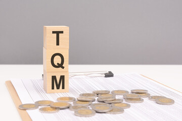 Sticker - wooden cubes on a brown background with the text TQM - an abbreviation for Total Quality Management. strong business concept