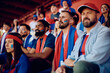 © Drazen - Group of male friends spectating sports game from stadium stands.