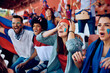 © Drazen - Happy woman and group of sports fans watching match at stadium.