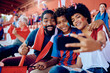© Drazen - Happy black family taking selfie with cell phone at stadium.