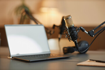 Close up shot of professional microphone with gold steel net and defocused white screen laptop on table in podcast room