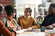 © Mediaphotos - Group of young African American students enjoying discussion sitting at table together in class, focus on girl smiling happily